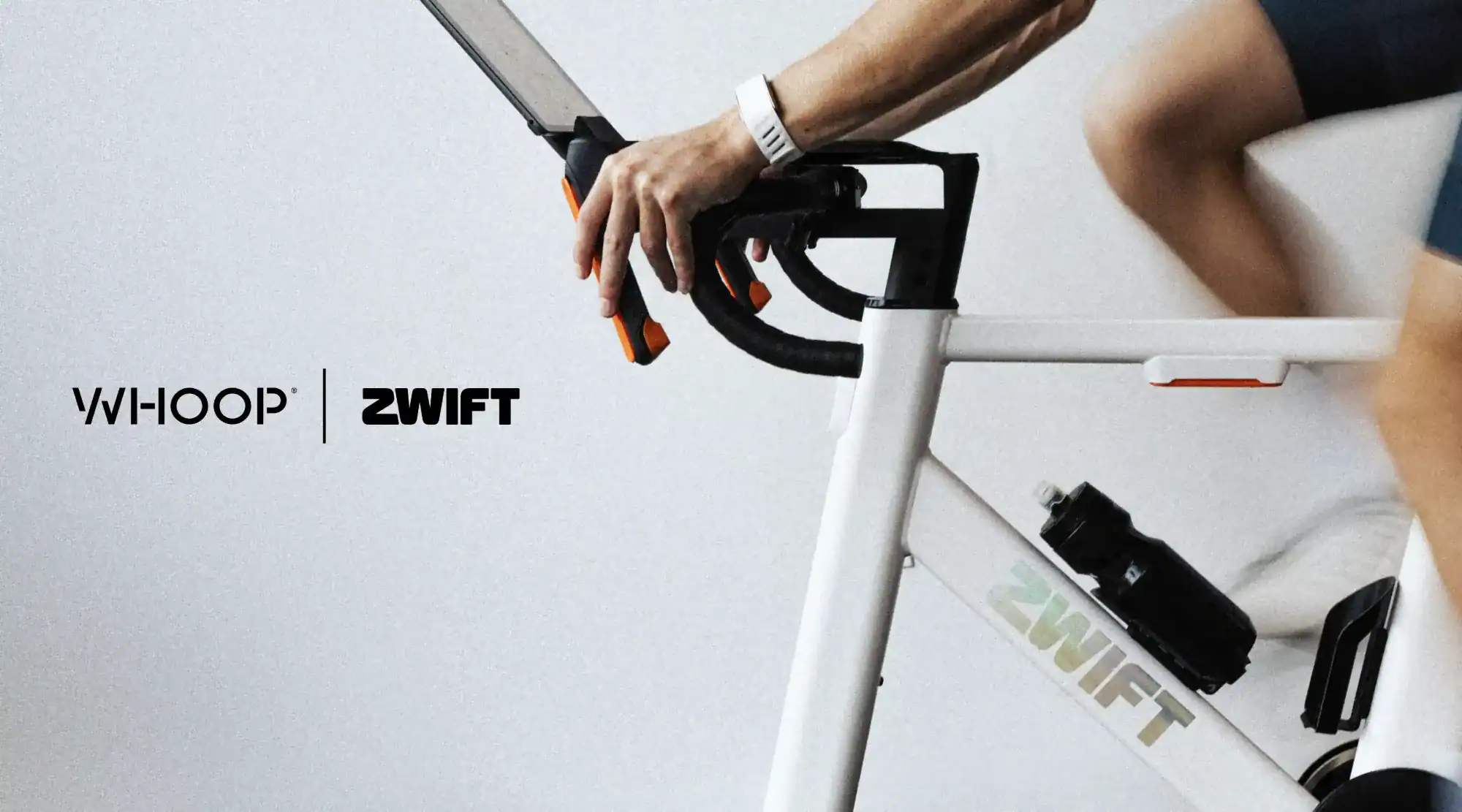 Integracja WHOOP i Zwift: logo WHOOP i ZWIFT obok rowerzysty na rowerze stacjonarnym Zwift Ride z białą opaską WHOOP na nadgarstku